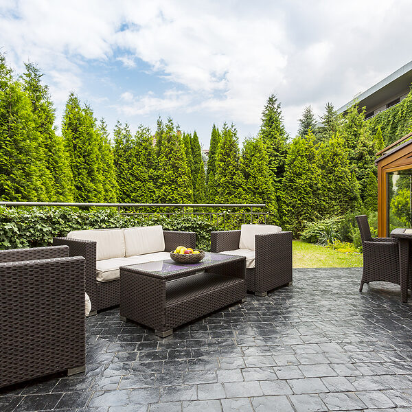 Large terrace patio with rattan garden furniture set surrounded by lush greenery
